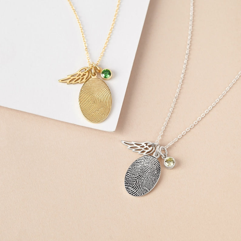 Two fingerprint necklaces, one gold and one silver, on a beige surface.