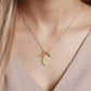 Gold necklace with a green gemstone pendant on a person wearing a beige top.