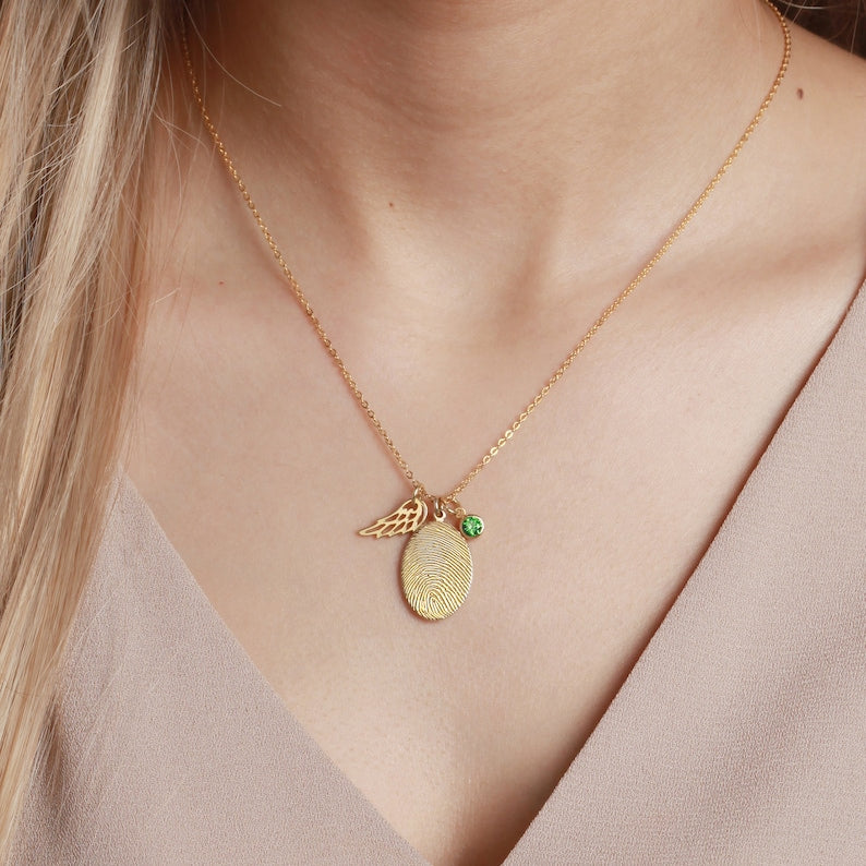 Gold necklace with a green gemstone pendant on a person wearing a beige top.