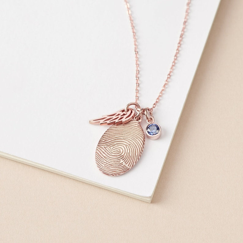 Rose gold fingerprint pendant necklace with a blue gemstone on a beige surface