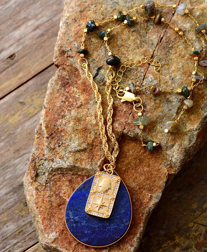 Gold necklace with a blue pendant on a stone surface