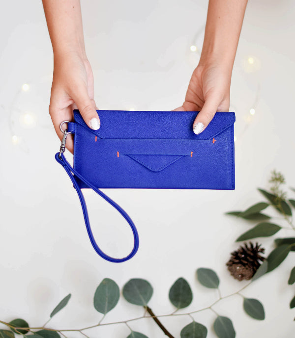 Blue clutch bag held by a person with a white background and green leaves.