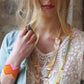 Woman wearing a gold necklace with colorful accents against a textured wall.