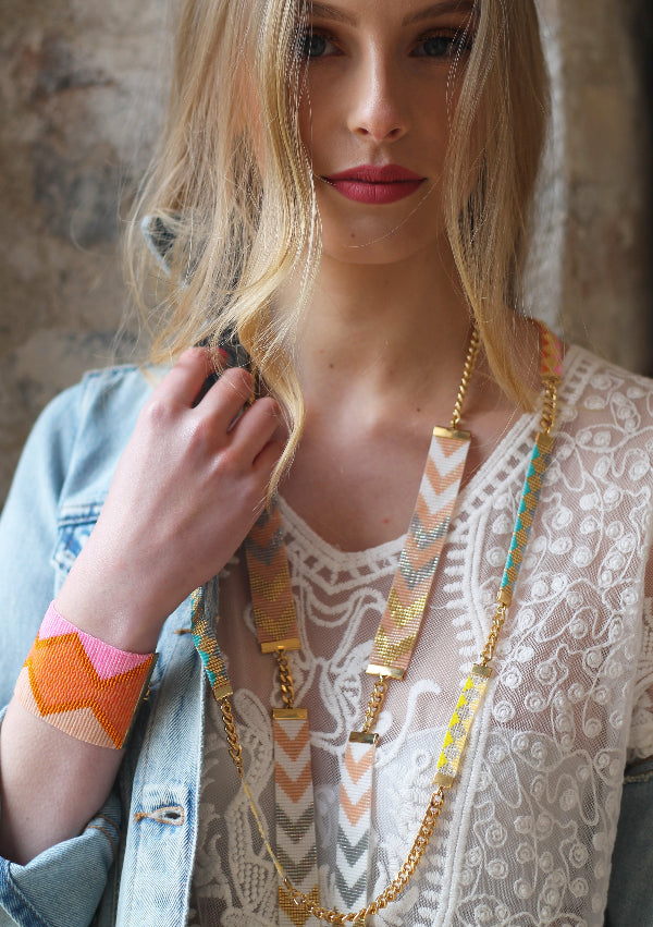 Woman wearing a gold necklace with colorful accents against a textured wall.
