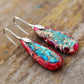 Pair of earrings with turquoise and red design on a wooden surface