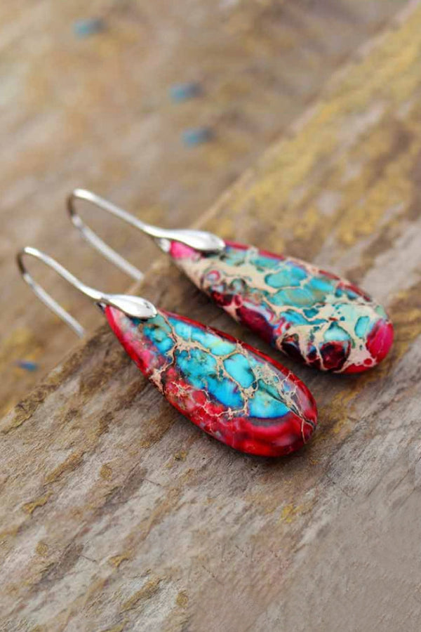 Pair of earrings with turquoise and red design on a wooden surface