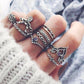 Hand wearing multiple silver rings with intricate designs on a textured fabric background