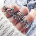 Hand wearing multiple silver rings with intricate designs on a textured fabric background