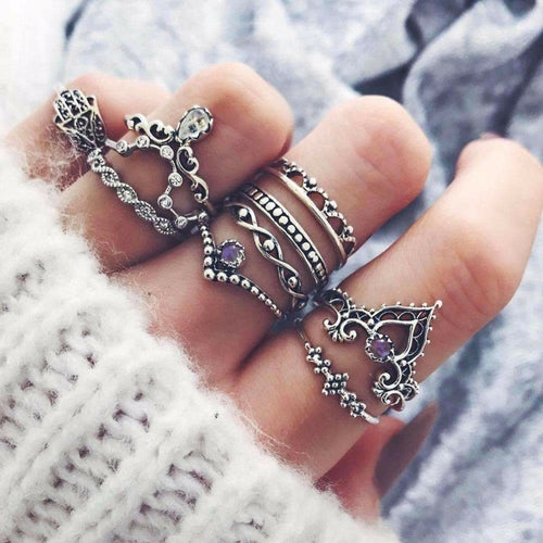 Hand wearing multiple silver rings with intricate designs on a textured fabric background