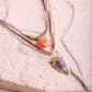 Two gold necklaces with gemstone pendants on a textured surface