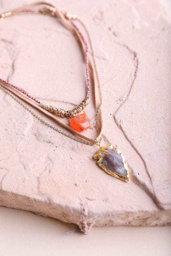 Two gold necklaces with gemstone pendants on a textured surface