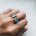 Hand wearing two rings with unique designs on a light background