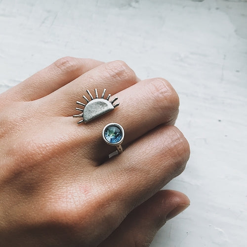 Hand wearing two rings with unique designs on a light background