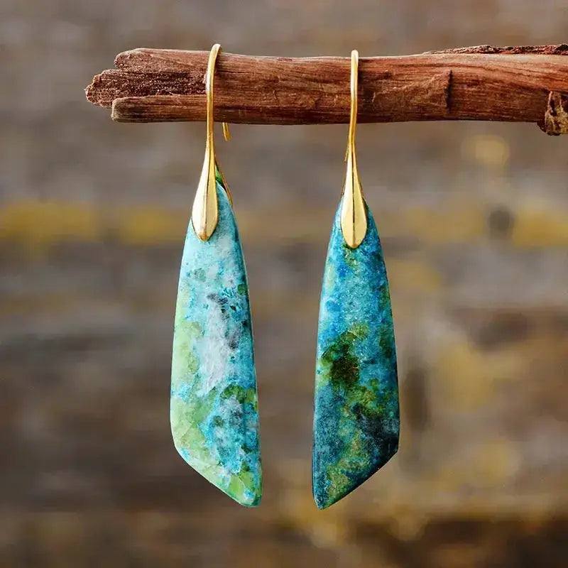Teal and gold earrings hanging on a branch with a blurred natural background
