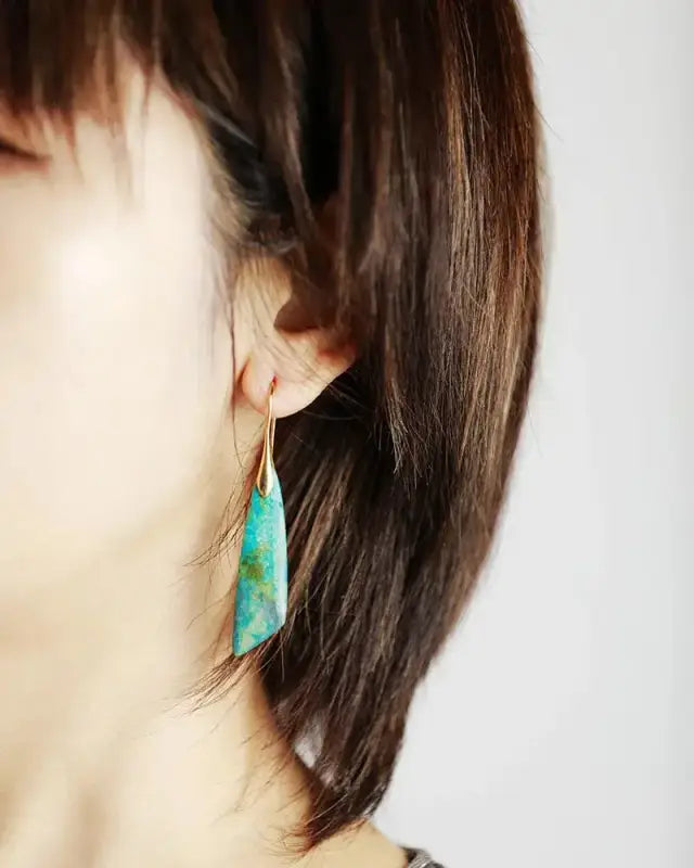 Close-up of a turquoise earring worn by a person with brown hair.