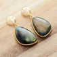 Gold earrings with green gemstones on a wooden surface
