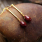 Gold earrings with red teardrop beads on a textured stone surface