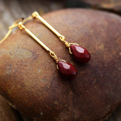 Gold earrings with red teardrop-shaped stones on a textured stone surface