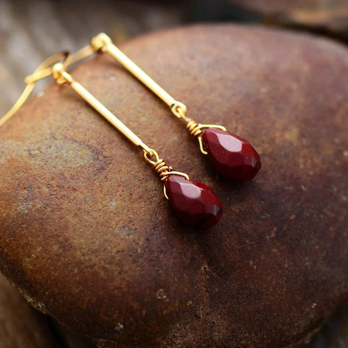 Gold earrings with red teardrop-shaped stones on a textured stone surface