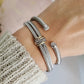 Close-up of a wrist wearing multiple silver bracelets on a neutral background