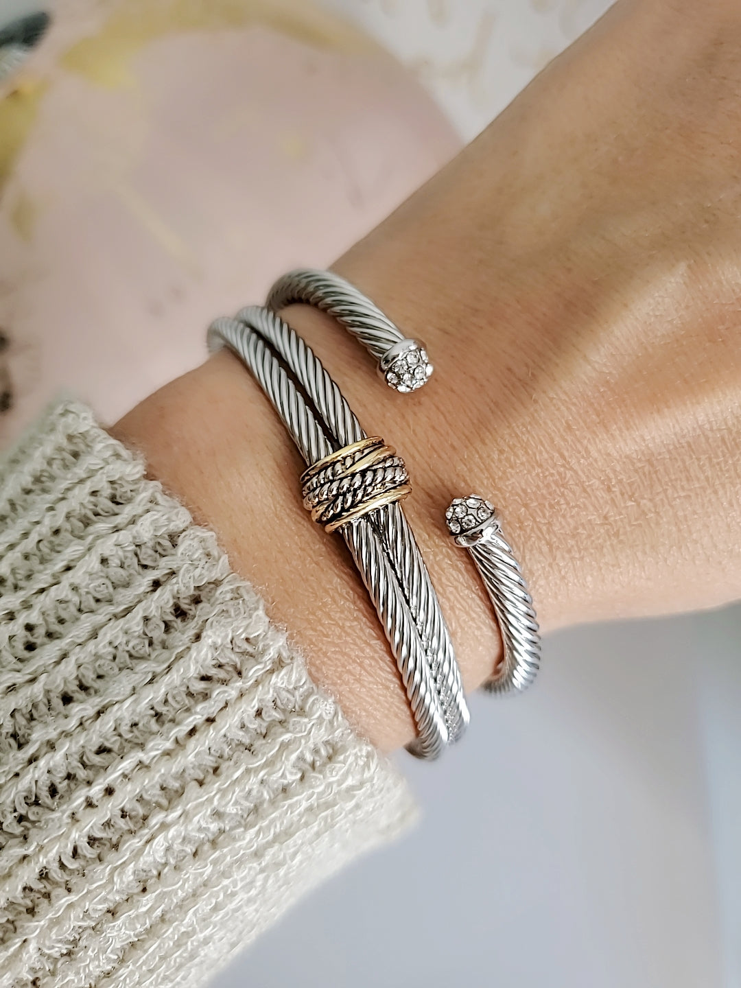 Close-up of a wrist wearing multiple silver bracelets on a neutral background