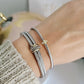 Close-up of a wrist wearing silver bracelets and gold rings on a neutral background