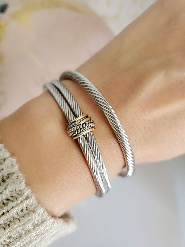Silver bracelet with gold accents on a wrist against a neutral background