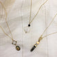 Three gold necklaces with various pendants on a textured beige fabric background