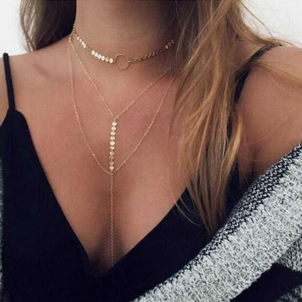 Gold body chain worn by a person with a black top and white and gray striped fabric.