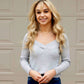 Woman wearing a light gray sweater with layered necklaces in front of a beige wall.