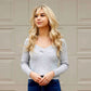 Woman with blonde hair wearing a light gray sweater and blue jeans against a beige wall.