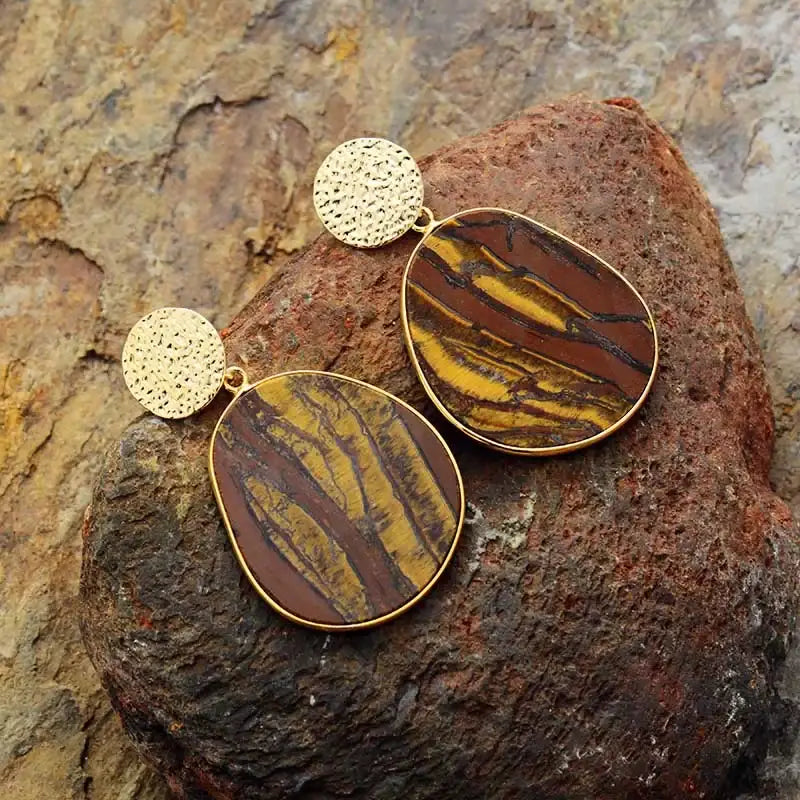 Gold and stone earrings on a textured rock surface