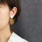Close-up of a person wearing gold earrings with a white shirt against a gray background