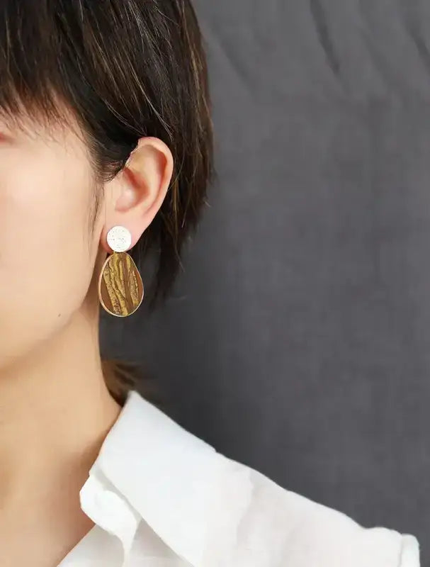 Close-up of a person wearing gold earrings with a white shirt against a gray background