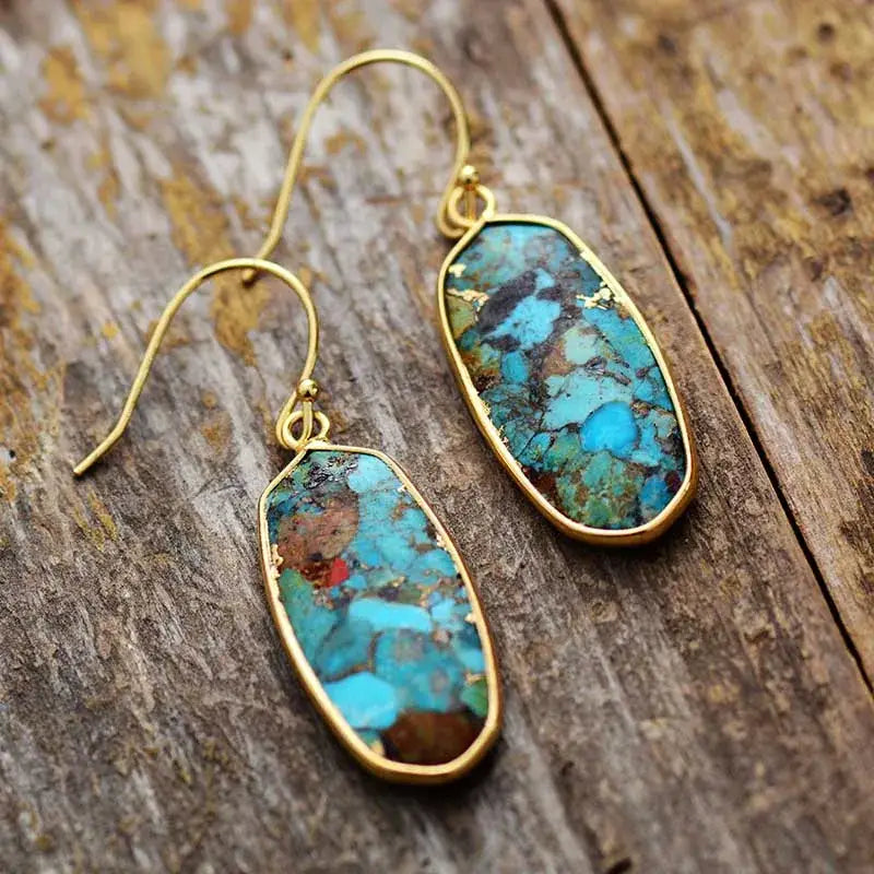 Turquoise stone earrings with gold hooks on a wooden surface