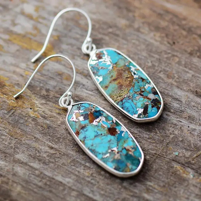 Turquoise stone earrings with silver hooks on a wooden surface