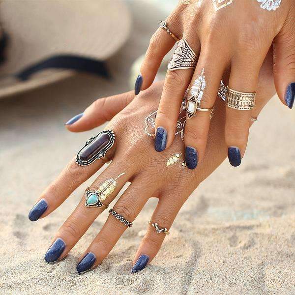 Close-up of a hand with multiple rings and blue nail polish on a blurred background