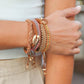 Close-up of a hand wearing multiple gold bracelets on a blurred background