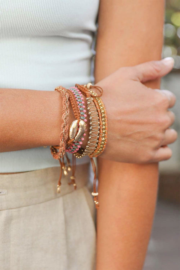 Close-up of a hand wearing multiple gold bracelets on a blurred background